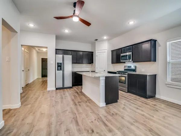 a large white kitchen with stainless steel appliances kitchen island a refrigerator sink and cabinets
