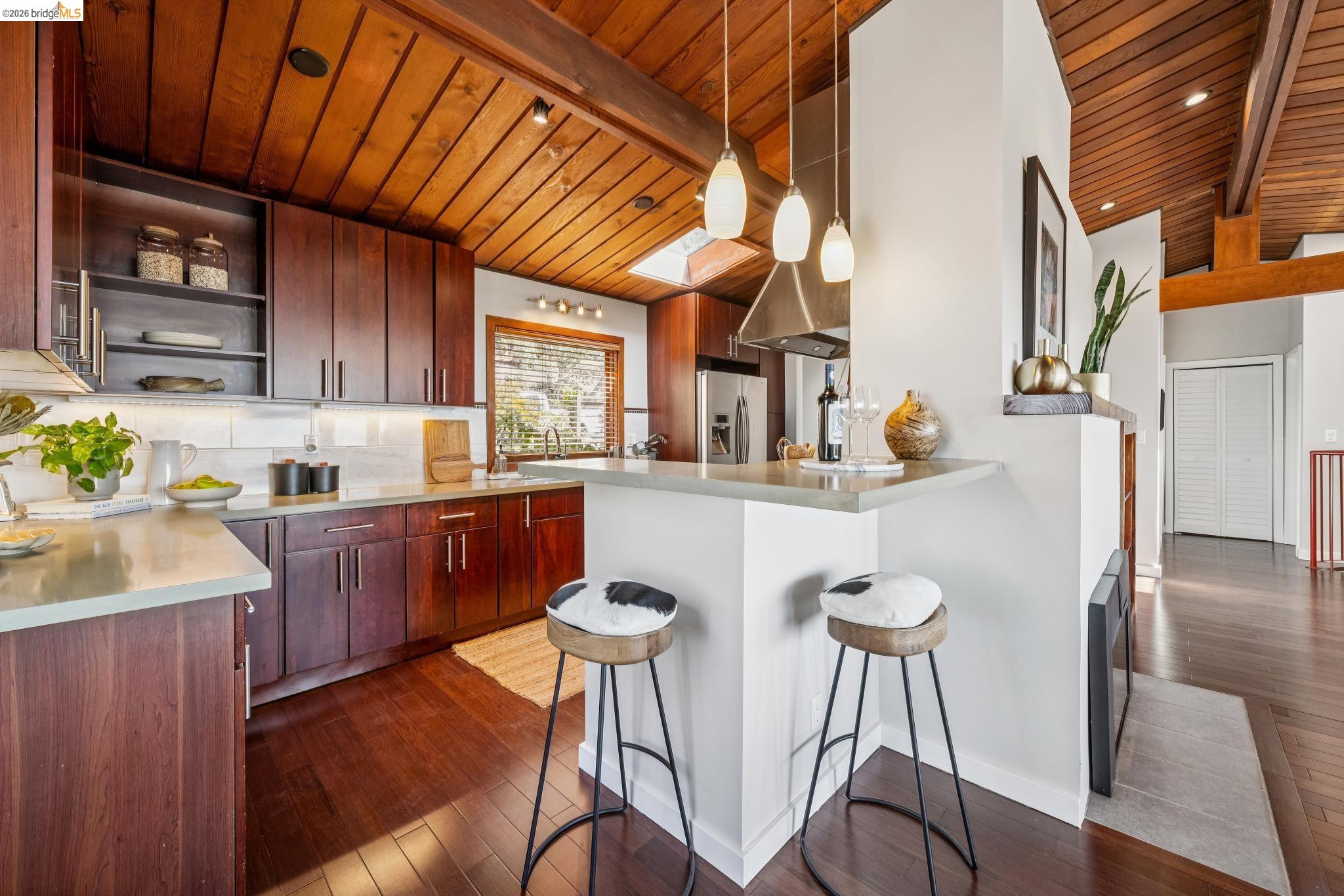 1394 Queens Road Berkeley, CA 94708 - Photo 10 of 63 Vaulted wood-finish ceiling with exposed beams, wood-finish flooring, dark wood-finish cabinetry, light-toned countertops, and stainless steel range hood