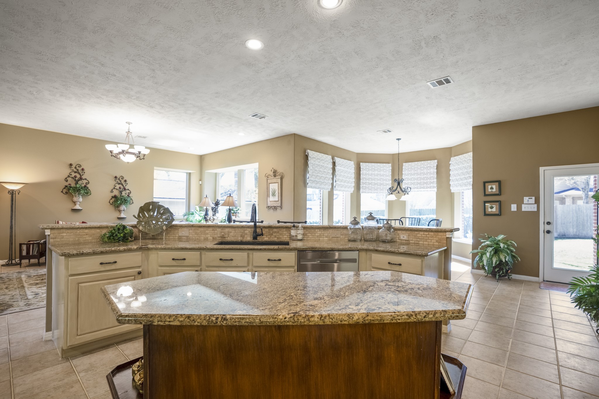 6615 Haughton Drive Spring, TX 77389 - Photo 13 of 50 Standing at the center island and looking outward, you can see how the kitchen opens toward the breakfast area beyond. The angled raised-bar island sits just in front, subtly defining the kitchen’s edge.
The breakfast area is wrapped in bay windows, surrounding the space with natural light and giving it a bright, almost sunroom-like feel. To the right, the back door provides easy access to the backyard.