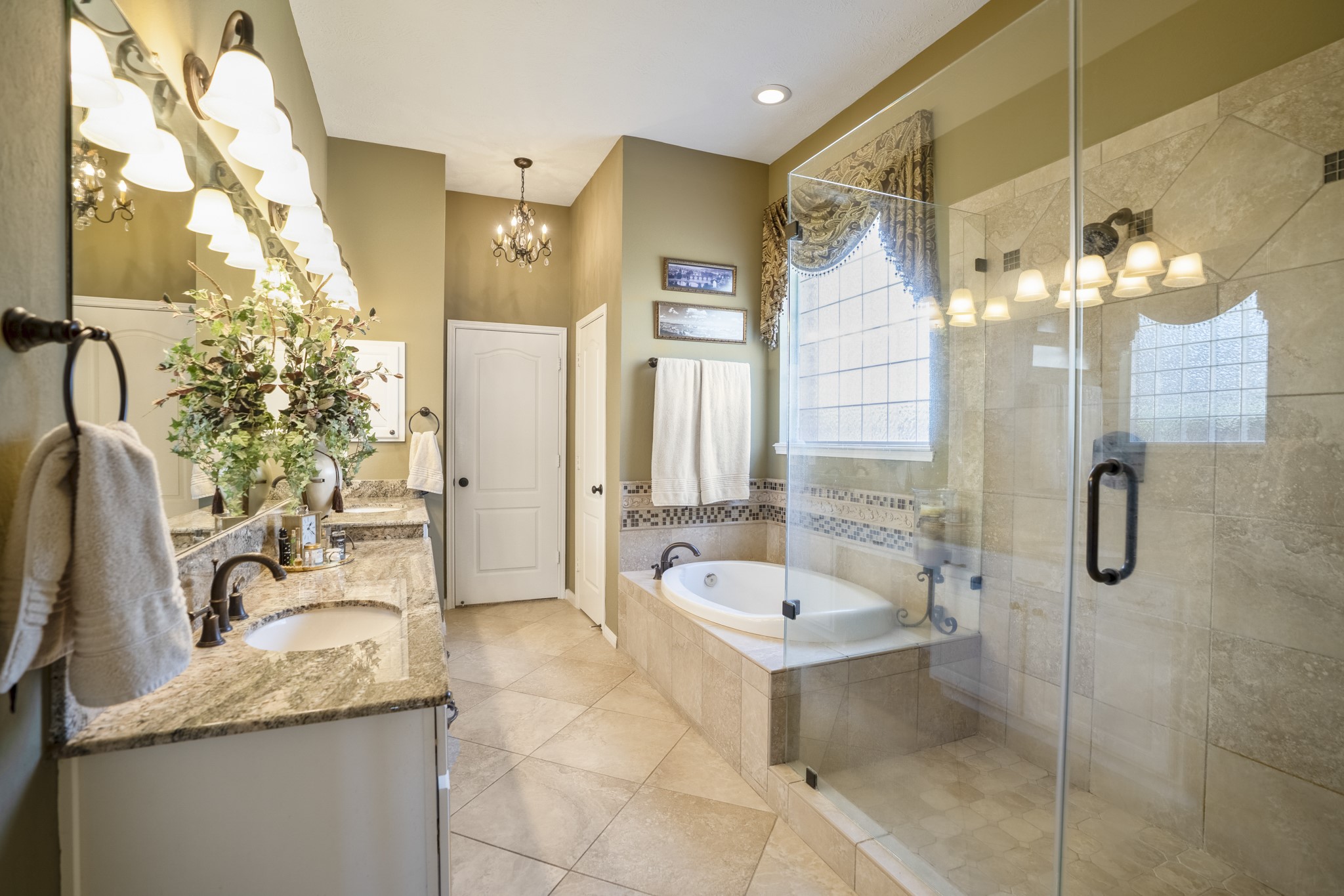 6615 Haughton Drive Spring, TX 77389 - Photo 20 of 50 Stepping into the primary bath, the space immediately feels elevated. A soaking tub rests beneath the window, framed by tile and natural light, while the glass-enclosed shower stands just beside it. The extended vanity stretches along the opposite wall with generous counter space and storage, creating a setting that feels polished and intentional.
It’s a bathroom that reads refined and indulgent — a true extension of the primary retreat.