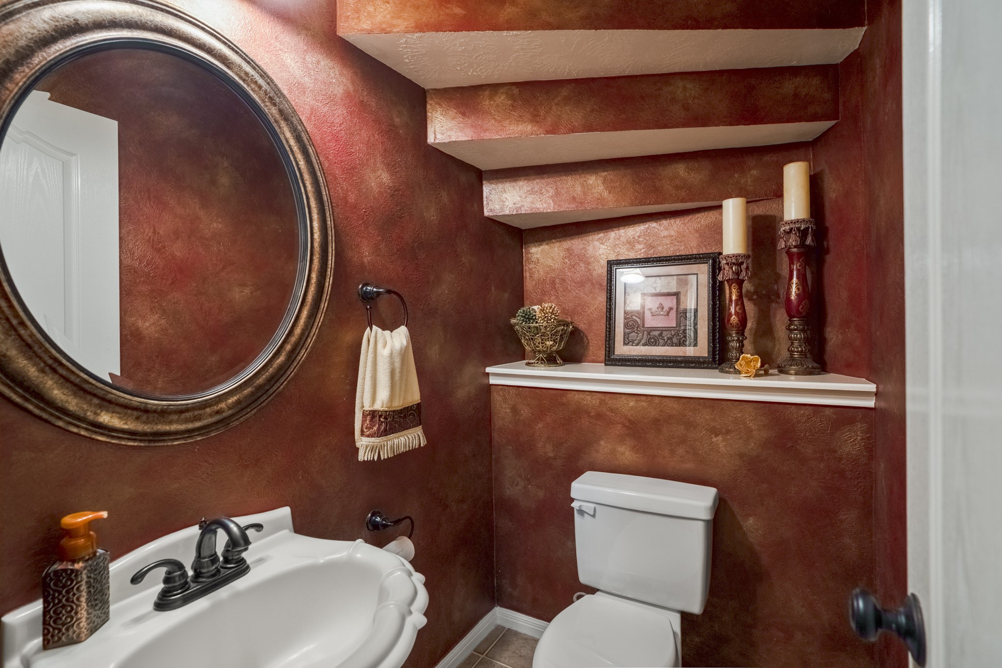 6615 Haughton Drive Spring, TX 77389 - Photo 23 of 50 Tucked beneath the curve of the staircase, the half bath makes a statement with its rich, vibrant walls and warm tones. The round mirror echoes the circular shape of the staircase above, adding a thoughtful design detail. It’s a space with personality — unexpected, memorable, and perfect for guests.