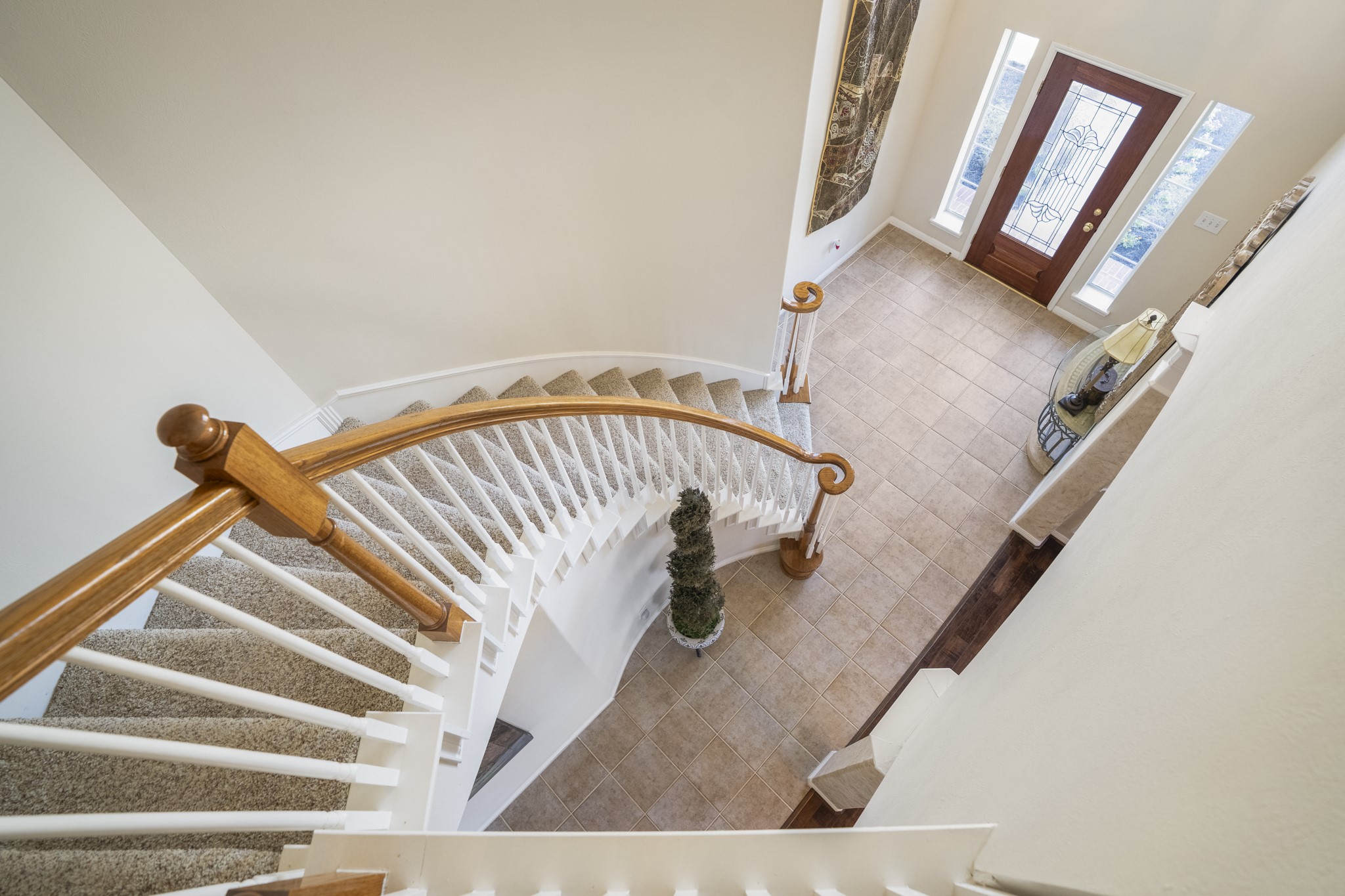 6615 Haughton Drive Spring, TX 77389 - Photo 24 of 50 Ascending the curved staircase, you can appreciate the craftsmanship up close. The wood handrail follows the sweep of the stairs, while the white balusters create a clean contrast against the warm tones below. From this vantage point, the two-story foyer opens beneath you, reinforcing the sense of height and openness at the entry.