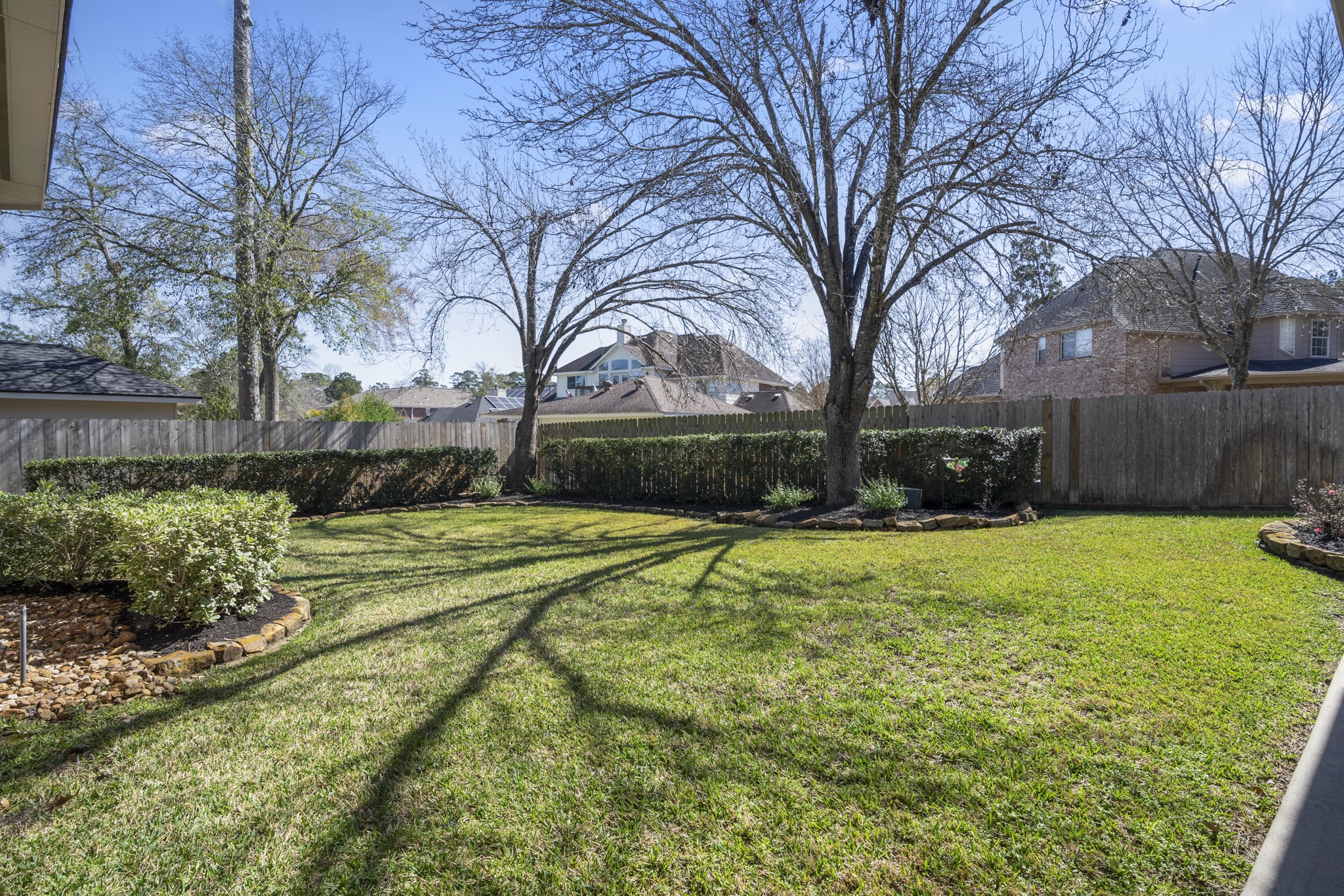6615 Haughton Drive Spring, TX 77389 - Photo 38 of 50 Turning around from the breezeway, the backyard opens into a wide stretch of green lawn with mature landscaping and established hedges along the fence line. A few well-placed trees add shade and character, while the open lawn gives the space a clean, usable feel. It’s a backyard that’s simple, well-kept, and ready to be enjoyed.