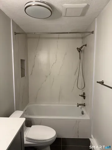 a bathroom with a granite countertop bathtub shower sink vanity and toilet