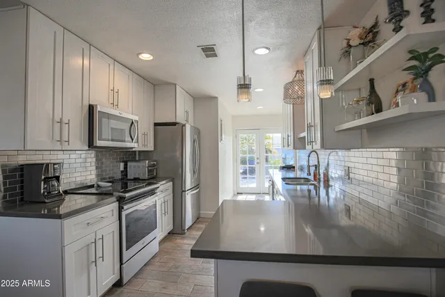 a kitchen with stainless steel appliances kitchen island granite countertop a stove a sink a refrigerator and white cabinets with wooden floor