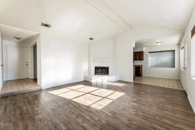 a view of empty room with wooden floor and kitchen view