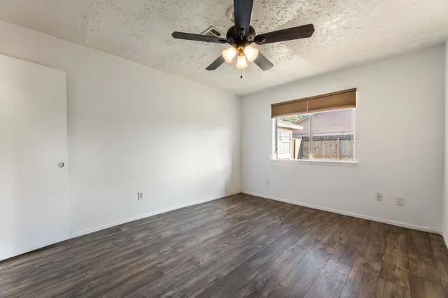 an empty room with wooden floor ceiling fan and windows