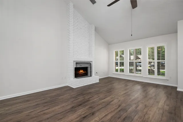a view of an empty room with wooden floor fireplace and a window