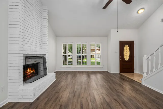 a view of an empty room with wooden floor fireplace and a window