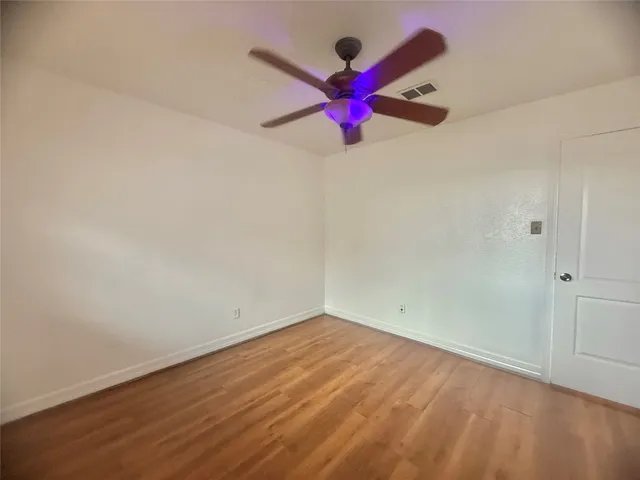 an empty room with wooden floor and fan