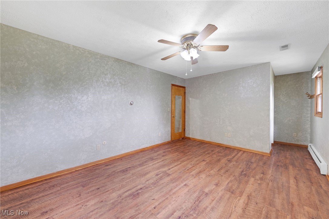 7923 Zigler Road Sterling, OH 44276 - Photo 17 of 31 Spare room featuring a baseboard radiator, wood finished floors, ceiling fan, a textured wall, and a textured ceiling