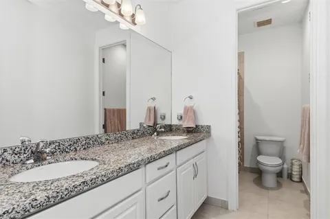 a bathroom with a granite countertop double vanity sink a toilet and a mirror