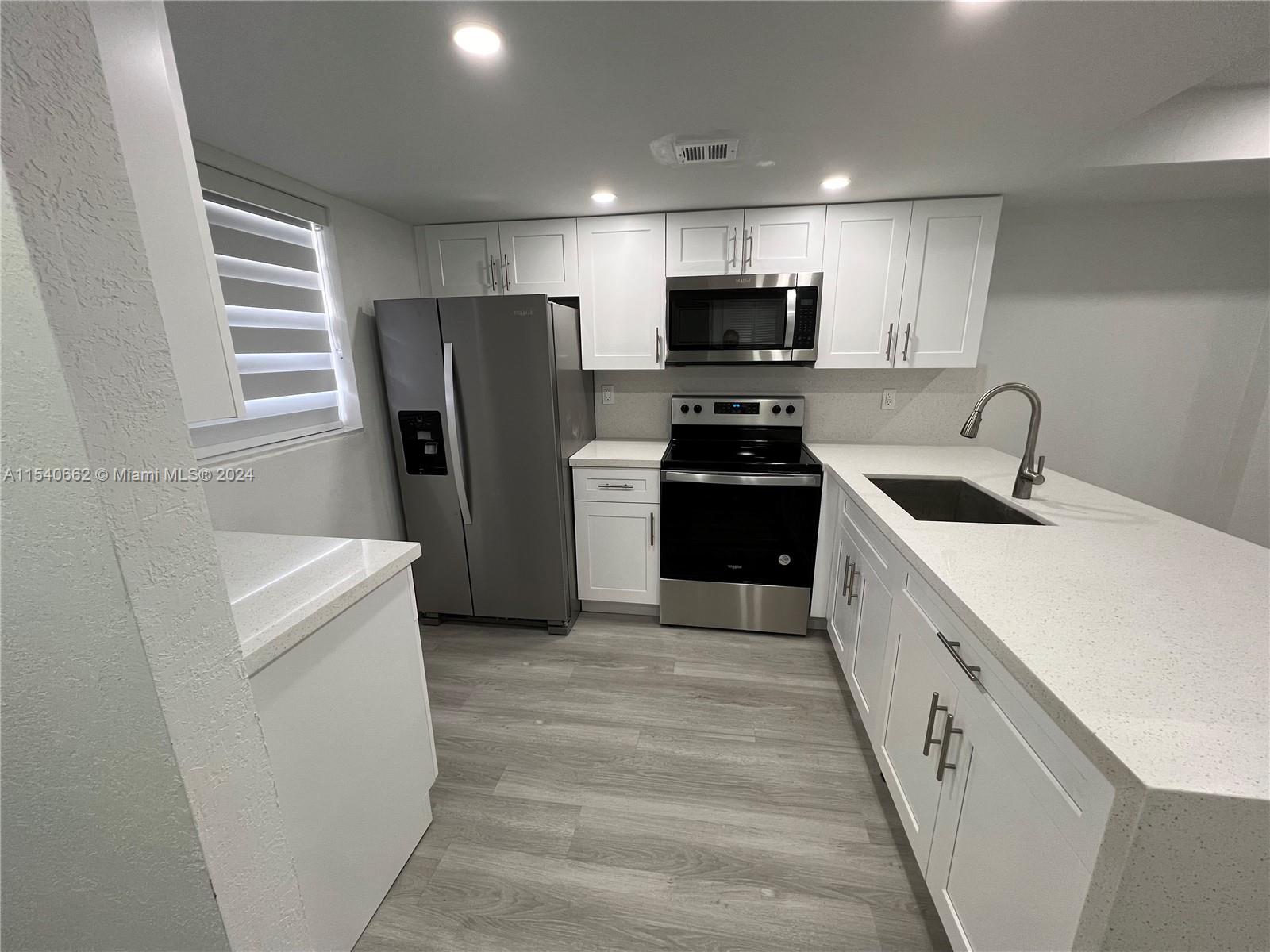 14155 Southwest 87th Street, Unit E108 Miami, FL 33183 - Photo 3 of 9 a kitchen with refrigerator a microwave and white cabinets