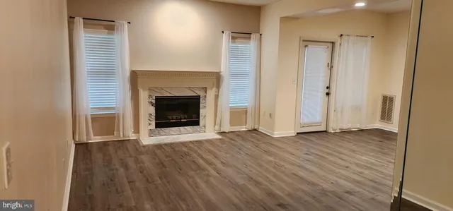 a view of an empty room with wooden floor fireplace and a window