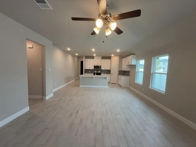 a view of a big room with wooden floor a kitchen view and a chandelier