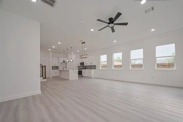 a view of an empty room with wooden floor and a ceiling fan