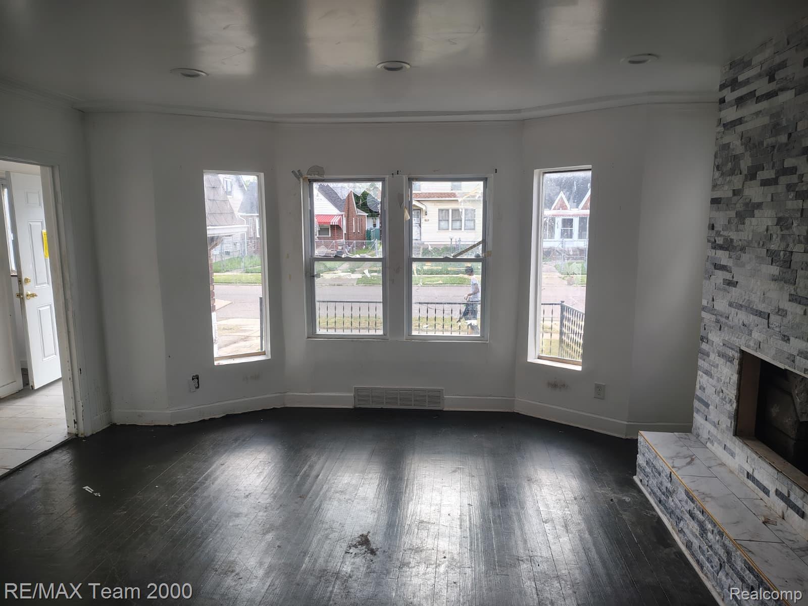 8860 Appoline Street Detroit, MI 48228 - Photo 7 of 45 Living area featuring a bay window with three sashed windows, dark wood-finish flooring, and a fireplace with a stacked stone facade and marble hearth