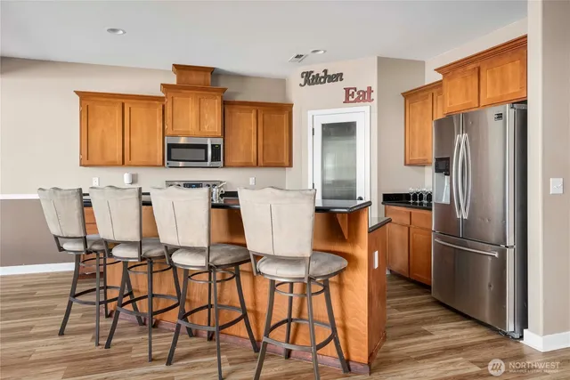 a kitchen with stainless steel appliances a refrigerator a stove a dining table and chairs with wooden floor