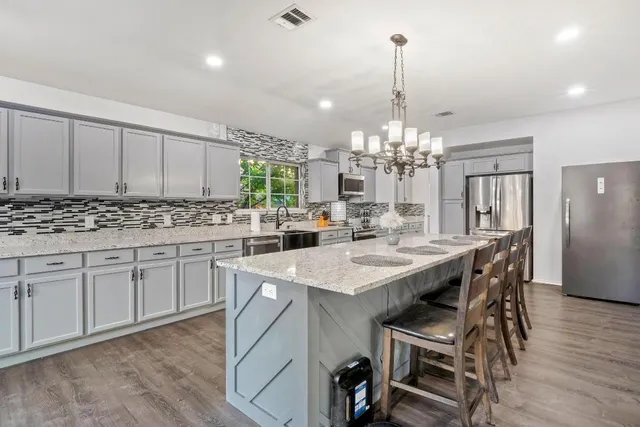 a kitchen with kitchen island granite countertop a center island a sink cabinets and a chandelier