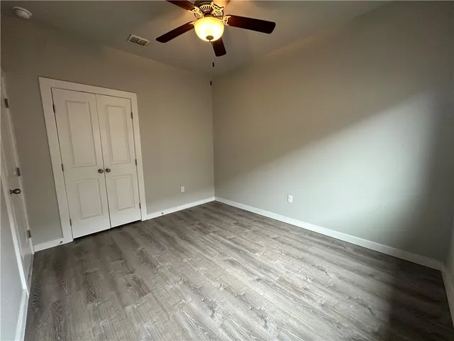 an empty room with wooden floor chandelier fan and windows