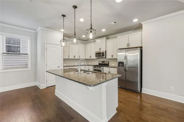 a kitchen with stainless steel appliances granite countertop a refrigerator a sink dishwasher a stove and white cabinets with wooden floor