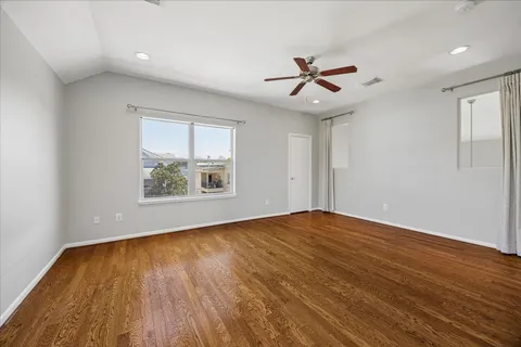an empty room with wooden floor chandelier fan and windows