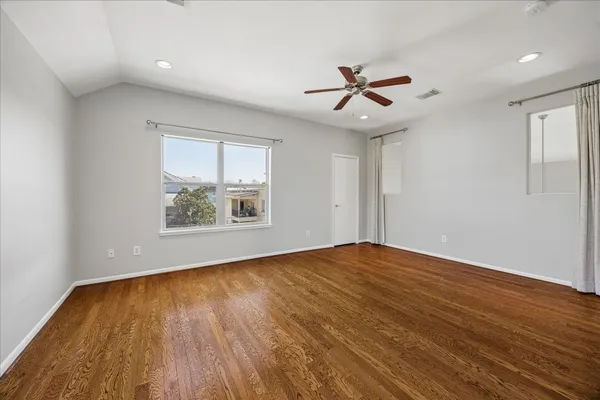 an empty room with wooden floor chandelier fan and windows
