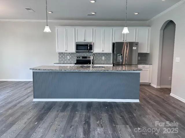 a kitchen with stainless steel appliances granite countertop a sink a stove a refrigerator cabinets and wooden floor