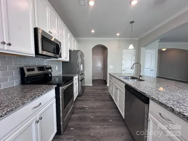 a large kitchen with stainless steel appliances kitchen island granite countertop a large counter top a stove a sink and a microwave