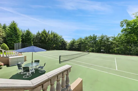 a view of a tennis court with table and chairs under an umbrella