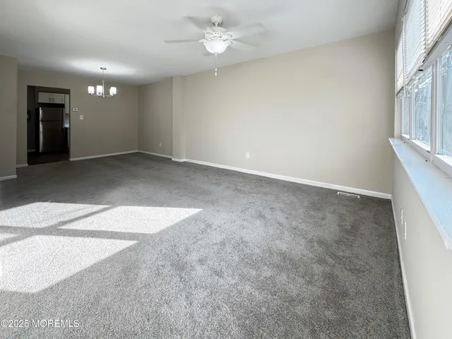 an empty room with chandelier fan and windows