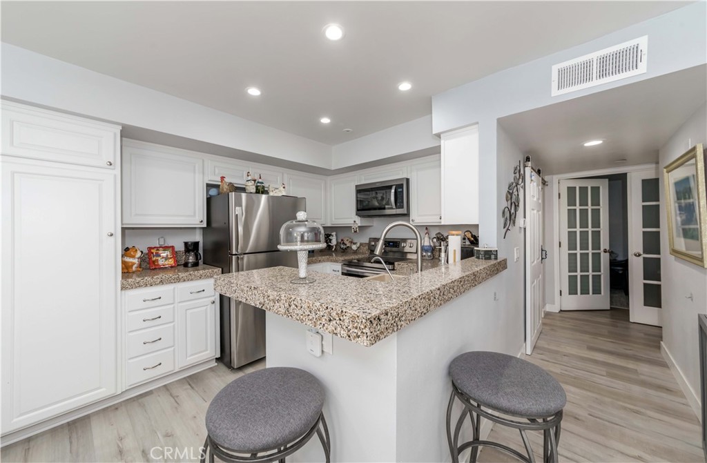 12671 Briarglen Loop, Unit G Stanton, CA 90680 - Photo 10 of 24 a kitchen with stainless steel appliances granite countertop a table chairs sink refrigerator and cabinets