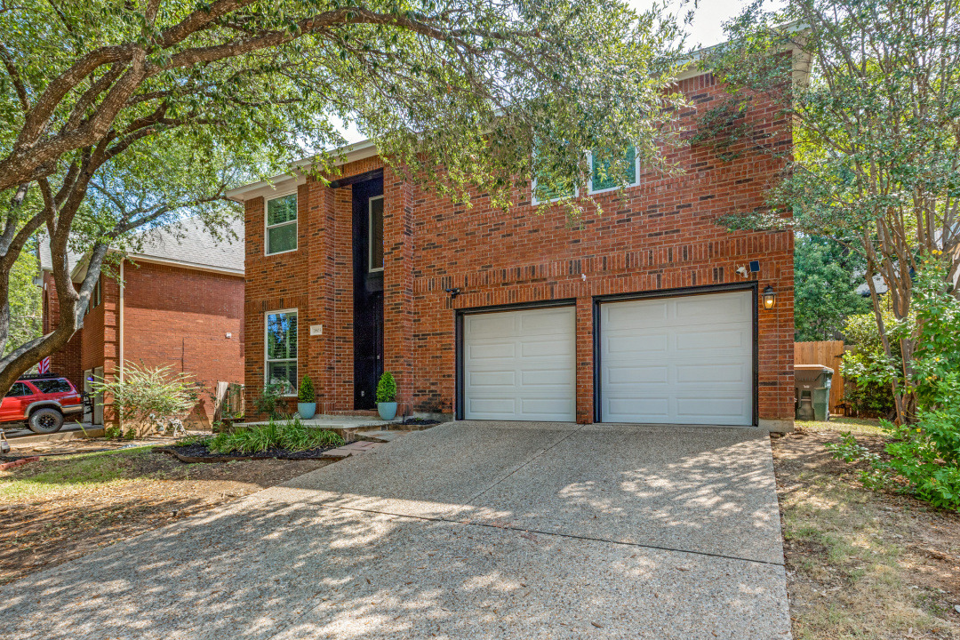 3803 Caney Creek Road Austin, TX 78732 - Photo 21 of 21 Mature trees shade a stately brick exterior featuring a two-car garage and concrete driveway.