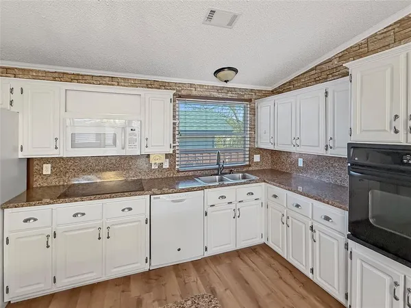 a kitchen with granite countertop a stove top oven a sink dishwasher and cabinets with wooden floor