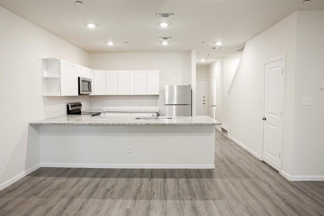 802 South 5th Street, Unit 1 Bonham, TX 75418 - Photo 21 of 25 Modern kitchen featuring white shaker cabinetry, stainless steel appliances, speckled countertops, and wood-finish flooring