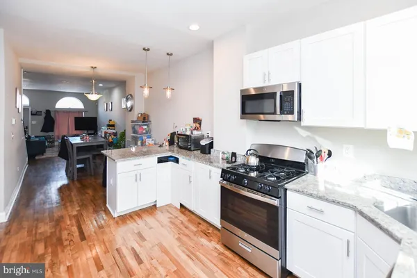 a kitchen with granite countertop a stove top oven a sink dishwasher and white cabinets with wooden floor