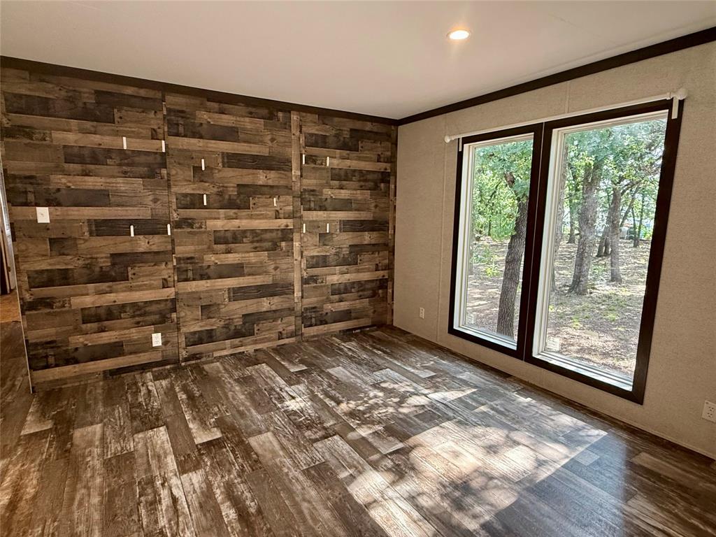 145 Adalida Lane Springtown, TX 76082 - Photo 7 of 29 Spacious room featuring wood-finish flooring, a prominent accent wall with varied wood paneling, and two large windows with dark trim providing ample natural light