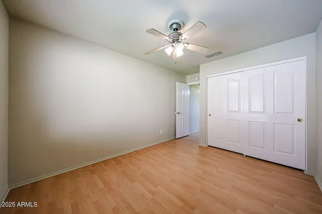 an empty room with wooden floor closet fan and windows