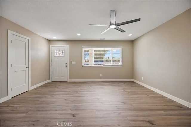 an empty room with wooden floor ceiling fan and windows