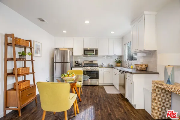 a kitchen with stainless steel appliances granite countertop a refrigerator a stove top oven a sink dishwasher and white cabinets with wooden floor
