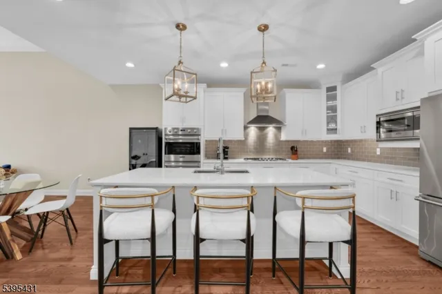 a kitchen with stainless steel appliances kitchen island granite countertop a refrigerator a stove a microwave oven a dining table and chairs with wooden floor