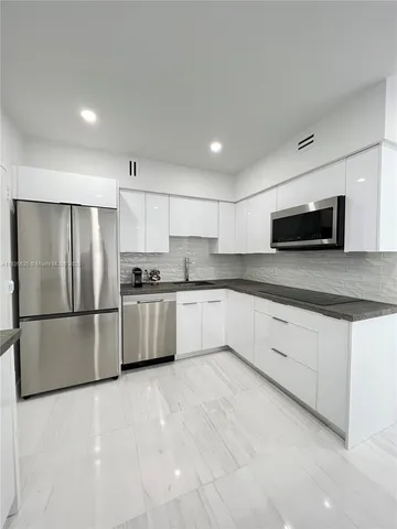 a kitchen with granite countertop a refrigerator a microwave a sink and white cabinets