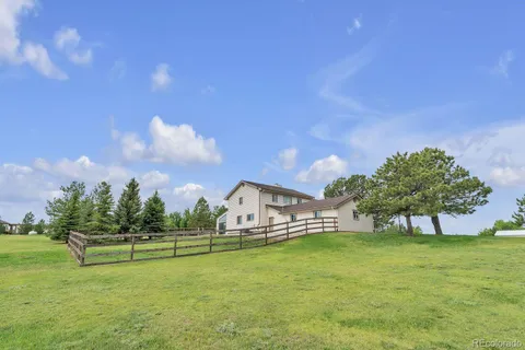 a white house with a big yard and a large trees with wooden fence