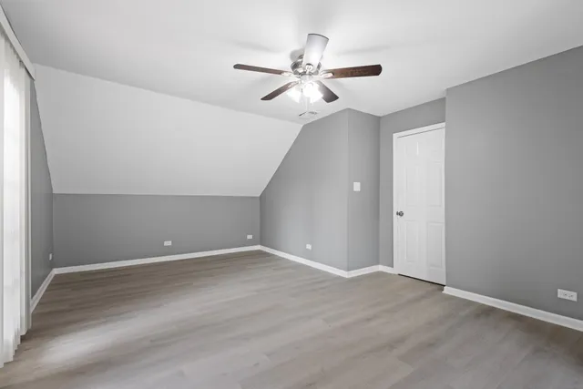 a view of an empty room with wooden floor and a ceiling fan