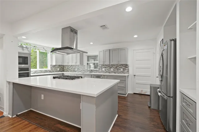 a large kitchen with a large counter top a sink stainless steel appliances and cabinets