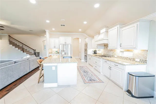 a large white kitchen with stainless steel appliances kitchen island granite countertop a large counter top a stove and a sink