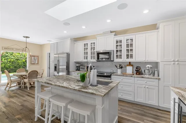 a kitchen with stainless steel appliances granite countertop a stove top oven a sink dishwasher a dining table and chairs with white cabinets