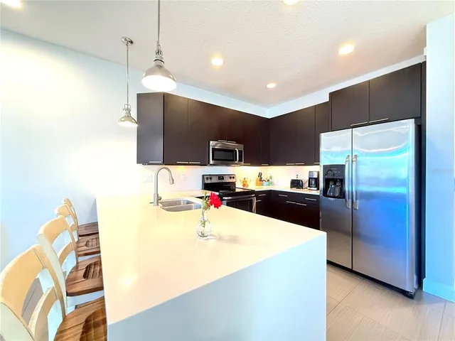 a kitchen with stainless steel appliances kitchen island a sink dishwasher a refrigerator with a dining table and chairs