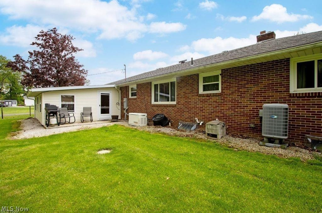 2530 Tuckahoe Road Wooster, OH 44691 - Photo 10 of 29 Expansive grassy yard alongside a brick exterior home featuring multiple windows, a white vinyl-sided addition, and a gravel patio area