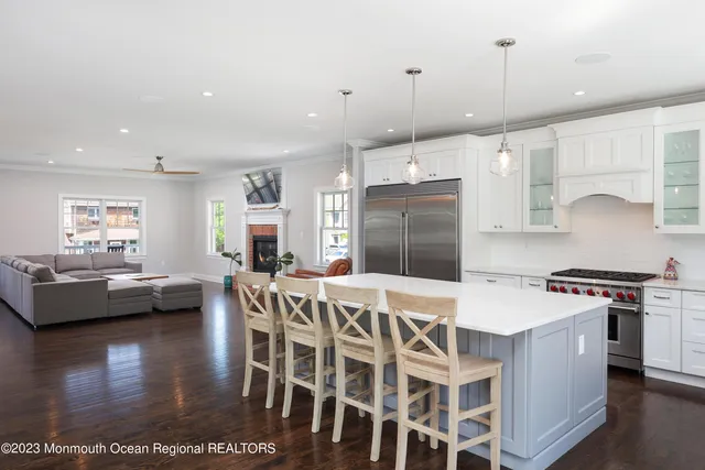 a kitchen with stainless steel appliances kitchen island granite countertop a stove a refrigerator a kitchen island a couches and chairs with wooden floor